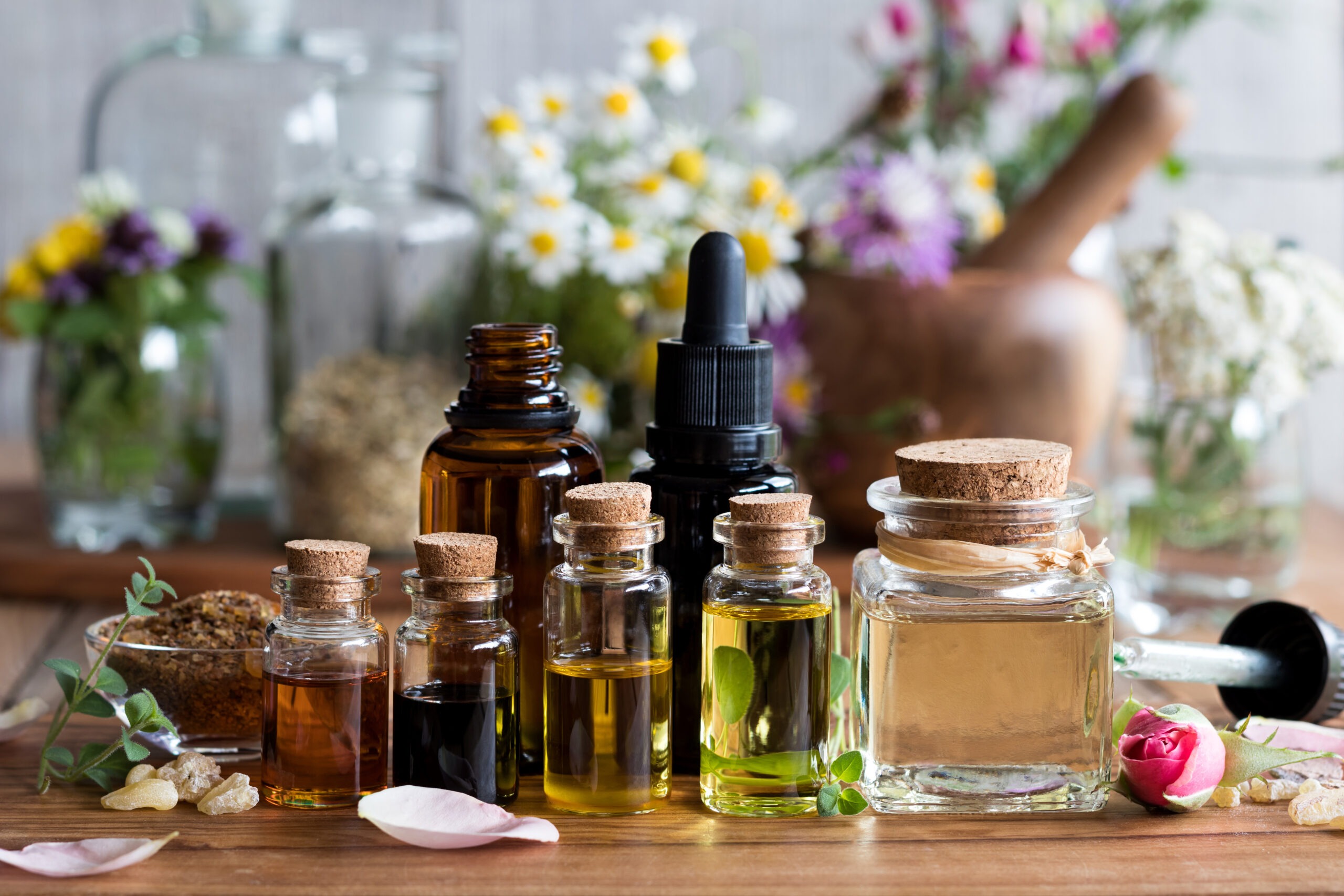 Glass bottles with essential oils on a wooden surface, surrounded by flowers and natural elements.
