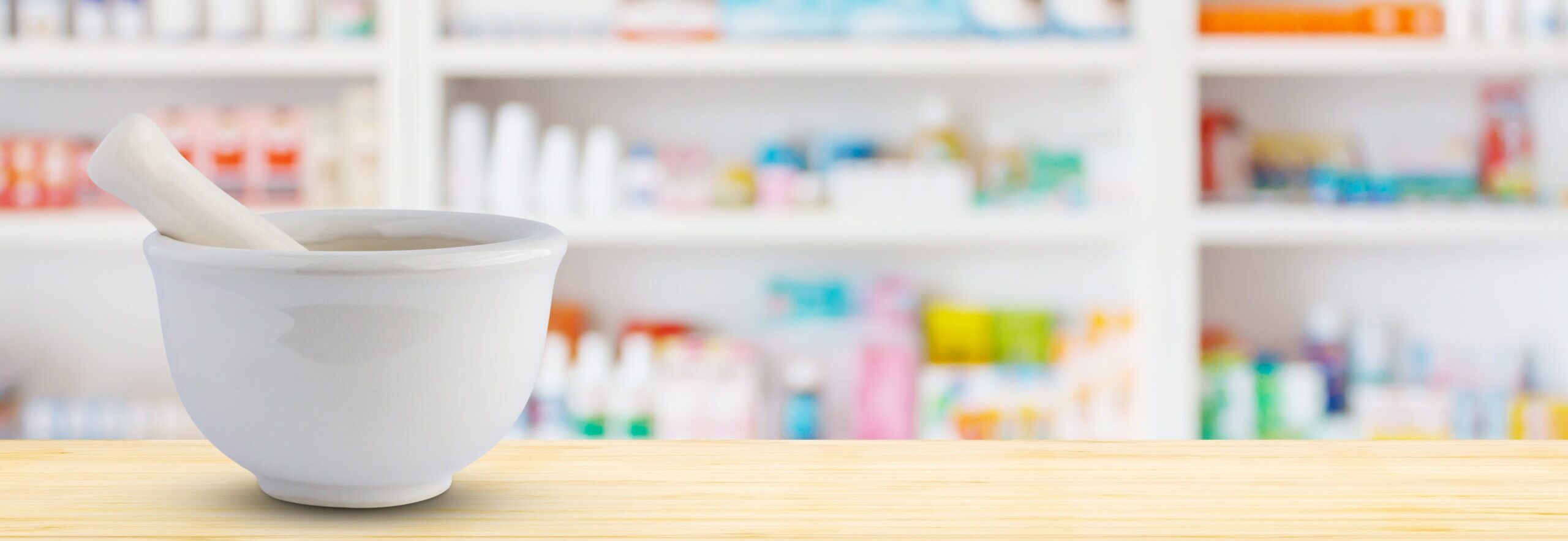 Mortar and pestle on a pharmacy counter with blurred shelves in the background.