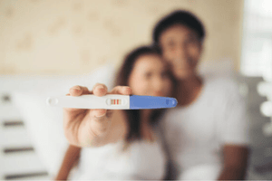 A person holding a positive pregnancy test with their partner in the background.