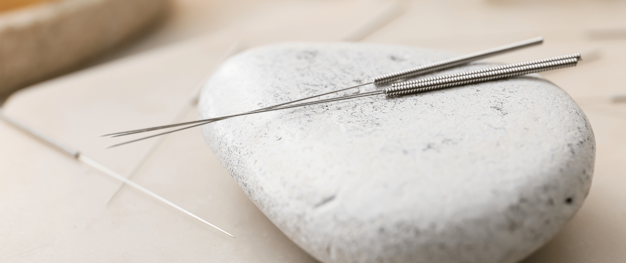 Acupuncture needles on a smooth white stone with a serene background.